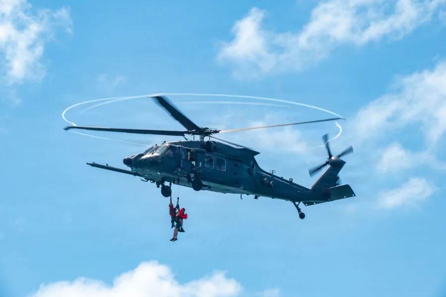 Black helicopter with two people hanging from a rope in a blue sky
