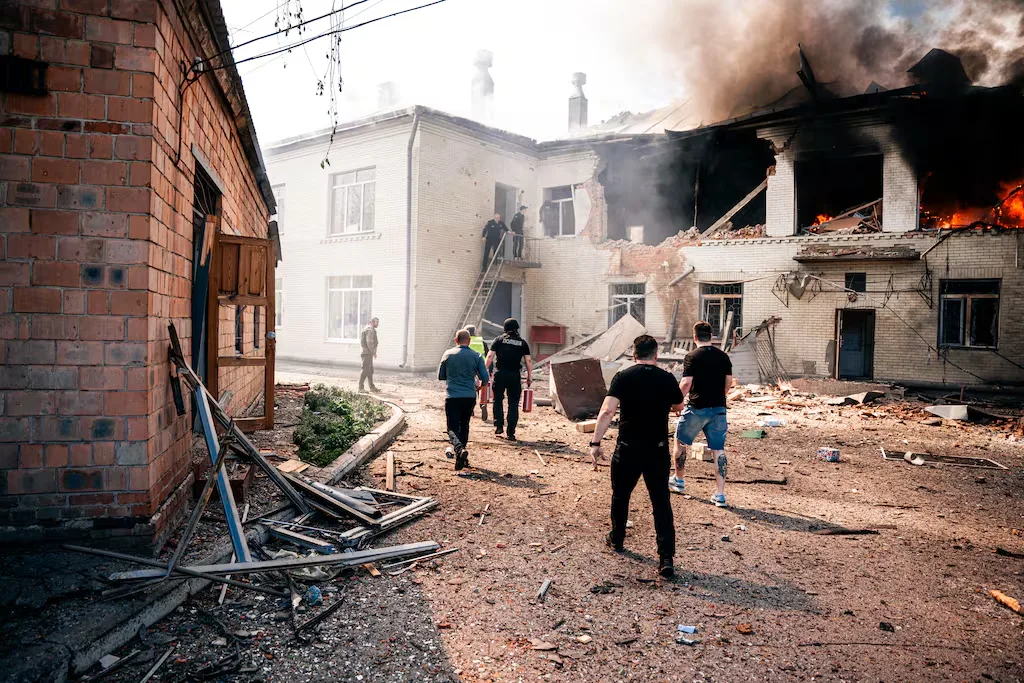 People in uniform run towards a burning building with smoke billowing from the roof.