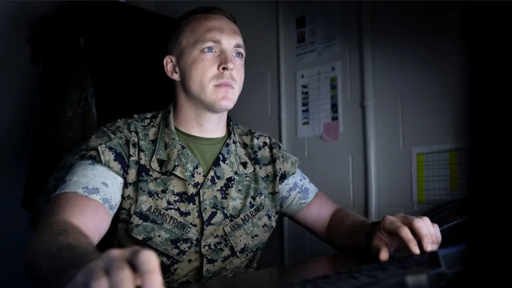 Marine wearing camouflage uniform sitting at desk working on computer