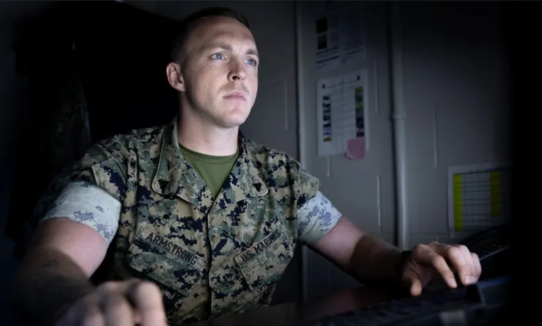 Marine wearing camouflage uniform sitting at desk working on computer