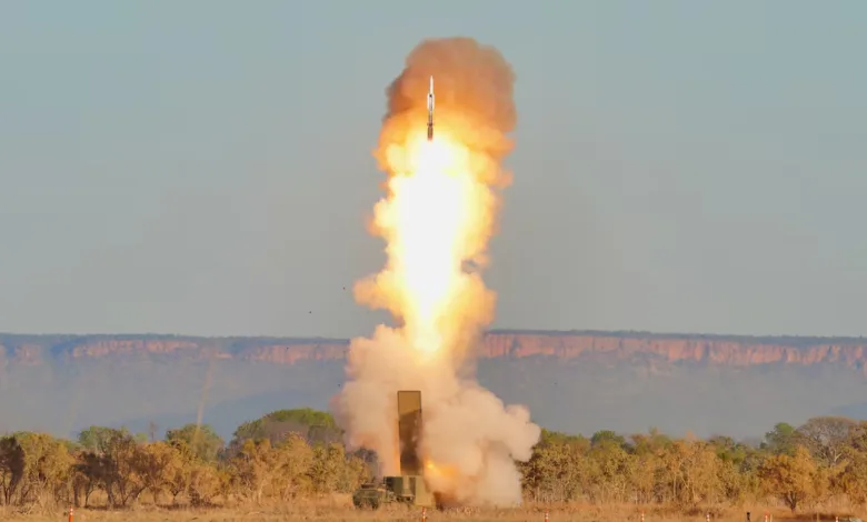 Missile launch from a mobile launcher with a bright plume of smoke and fire against a clear sky.
