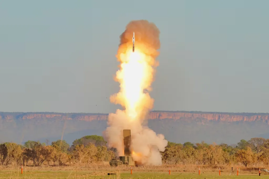 Missile launch from a mobile launcher with a bright plume of smoke and fire against a clear sky.
