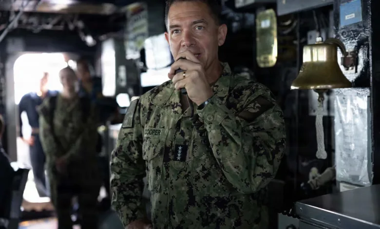 Navy Commander Cooper in uniform speaks on a ship, with crew in background.