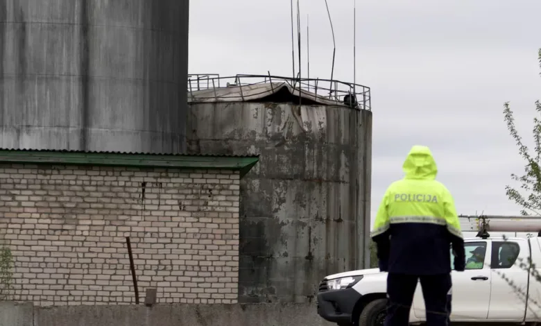 Police officer in yellow vest near damaged industrial tanks