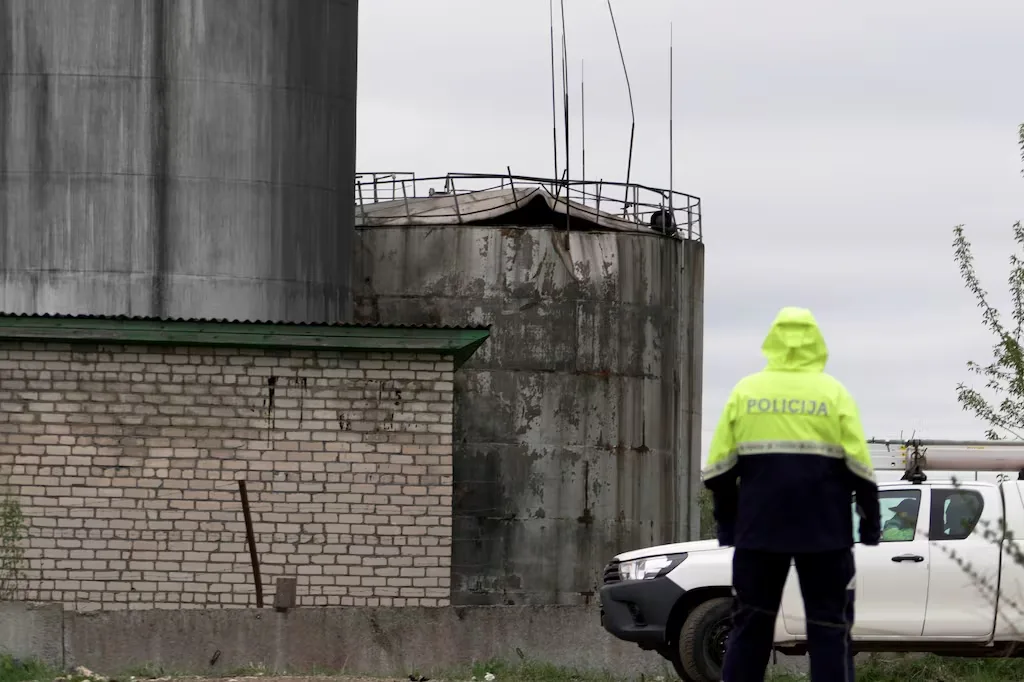 Police officer in yellow vest near damaged industrial tanks