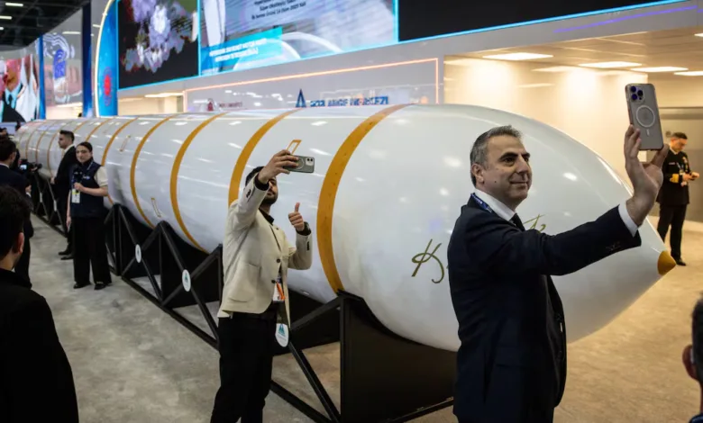 Men take photos of a large white rocket stage with gold stripes at an exhibition.