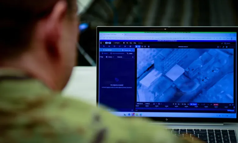 Soldier reviews drone footage on a laptop showing an aerial view of buildings.