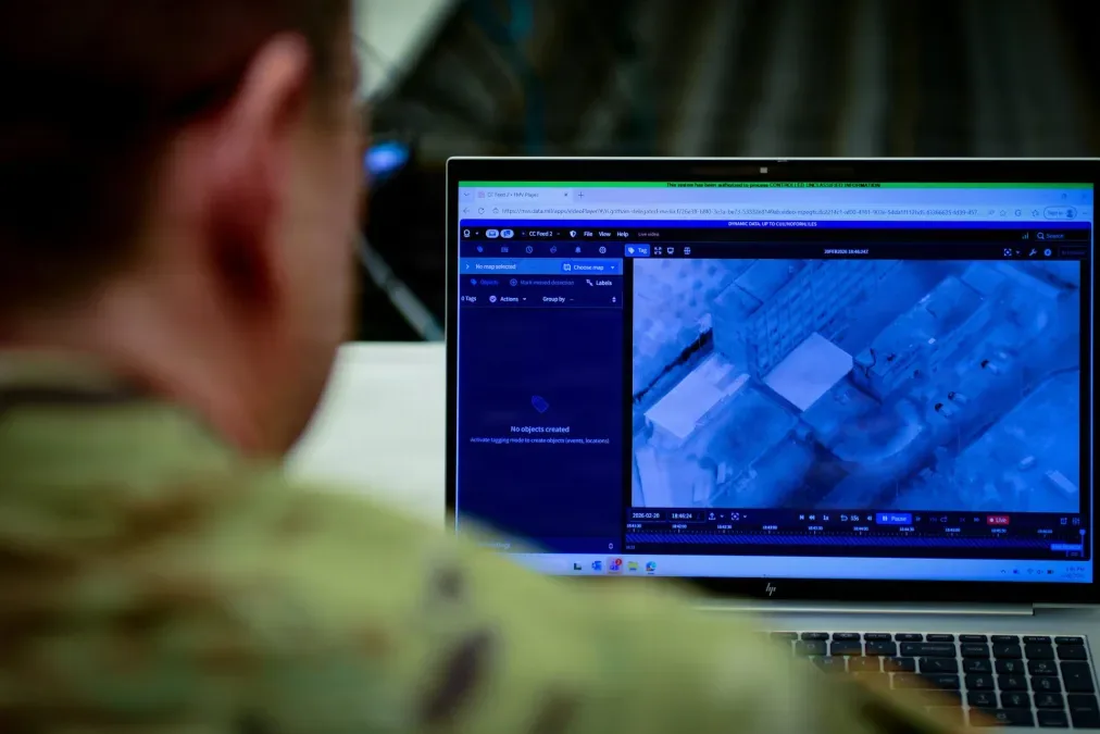 Soldier reviews drone footage on a laptop showing an aerial view of buildings.