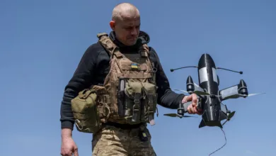 Ukrainian soldier holds a black drone with white markings against a blue sky.
