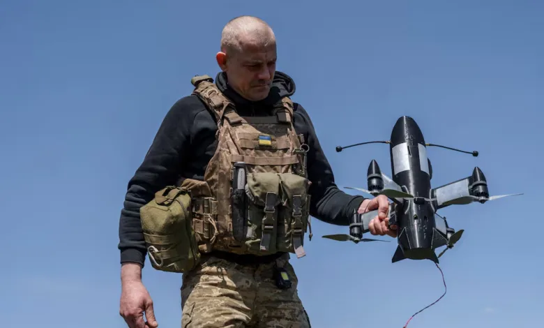 Ukrainian soldier holds a black drone with white markings against a blue sky.