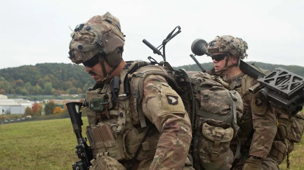 US soldiers in tactical gear walk outdoors with backpacks and equipment.