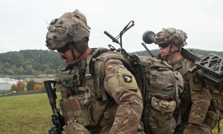 US soldiers in tactical gear walk outdoors with backpacks and equipment.