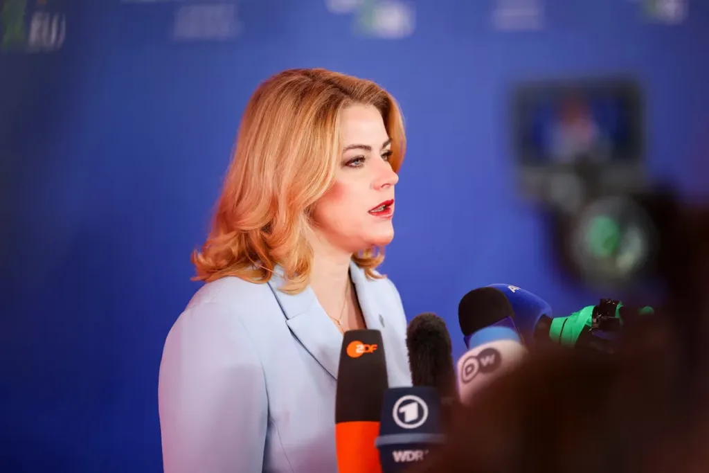 Woman in blue suit speaking at a press conference with microphones