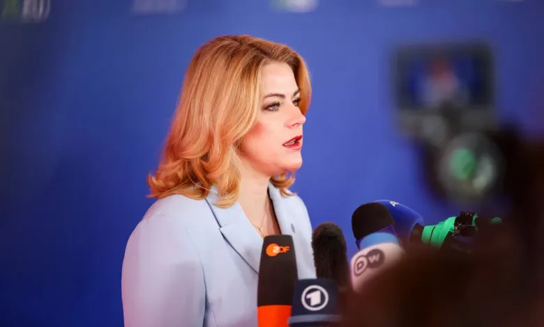 Woman in blue suit speaking at a press conference with microphones